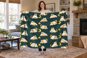 Woman holding an open Moonlit Mischief blanket with orange tabby cats in ghost costumes, golden moons, and stars on teal.
