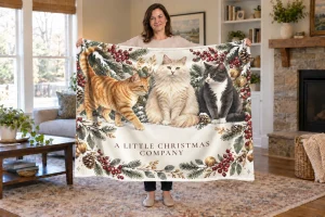 Woman holding an open Christmas cat blanket with three cats and A Little Christmas Company printed below them.