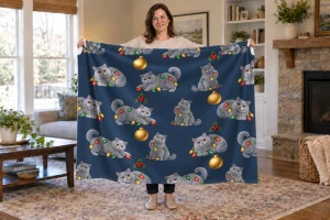 Woman holding an open Tangled in Lights blanket with gray cats, colorful Christmas lights, and gold ornaments on navy.