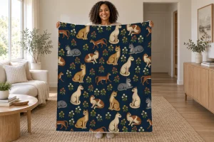 Woman holding open a navy blanket with cream, gray, gold, and russet cats among red, gold, and ivory flowers in a bright room.