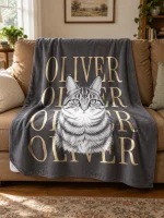 Graphite personalized cat blanket draped over a sofa, with a pencil-style tabby portrait over rows of the name OLIVER.