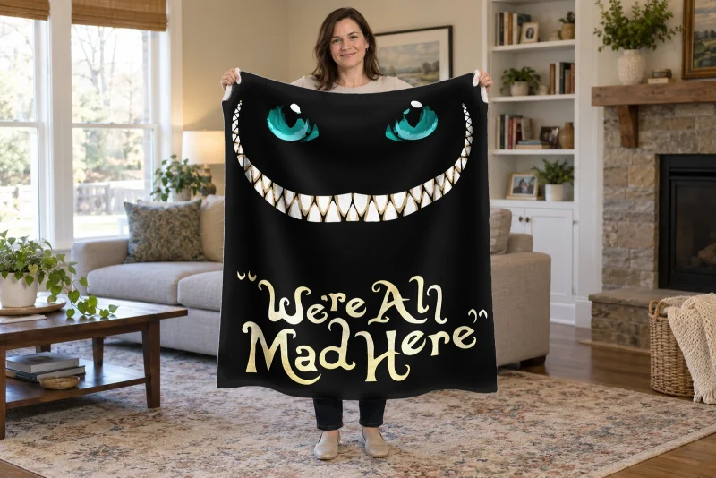 Man holding open a black cat blanket with turquoise eyes, a wide white grin, and the quote We're All Mad Here.
