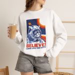 Person wearing a crewneck sweatshirt showing a gray tabby astronaut, a ringed golden planet and stars on deep blue Person wearing a crewneck sweatshirt showing a gray tabby astronaut, a ringed golden planet and stars on deep blue