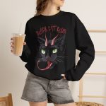 Person wearing a crewneck sweatshirt showing a horned black cat with green eyes, a curling red tongue and angular red lettering