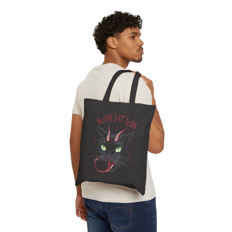Person carrying a black canvas tote showing a horned black cat with green eyes, a curling red tongue and angular red lettering