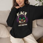 Person wearing a hoodie showing a grinning black cat with huge green eyes, orange mouth outlines and a purple halo