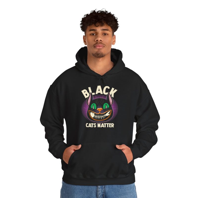 Person wearing a hoodie showing a grinning black cat with huge green eyes, orange mouth outlines and a purple halo