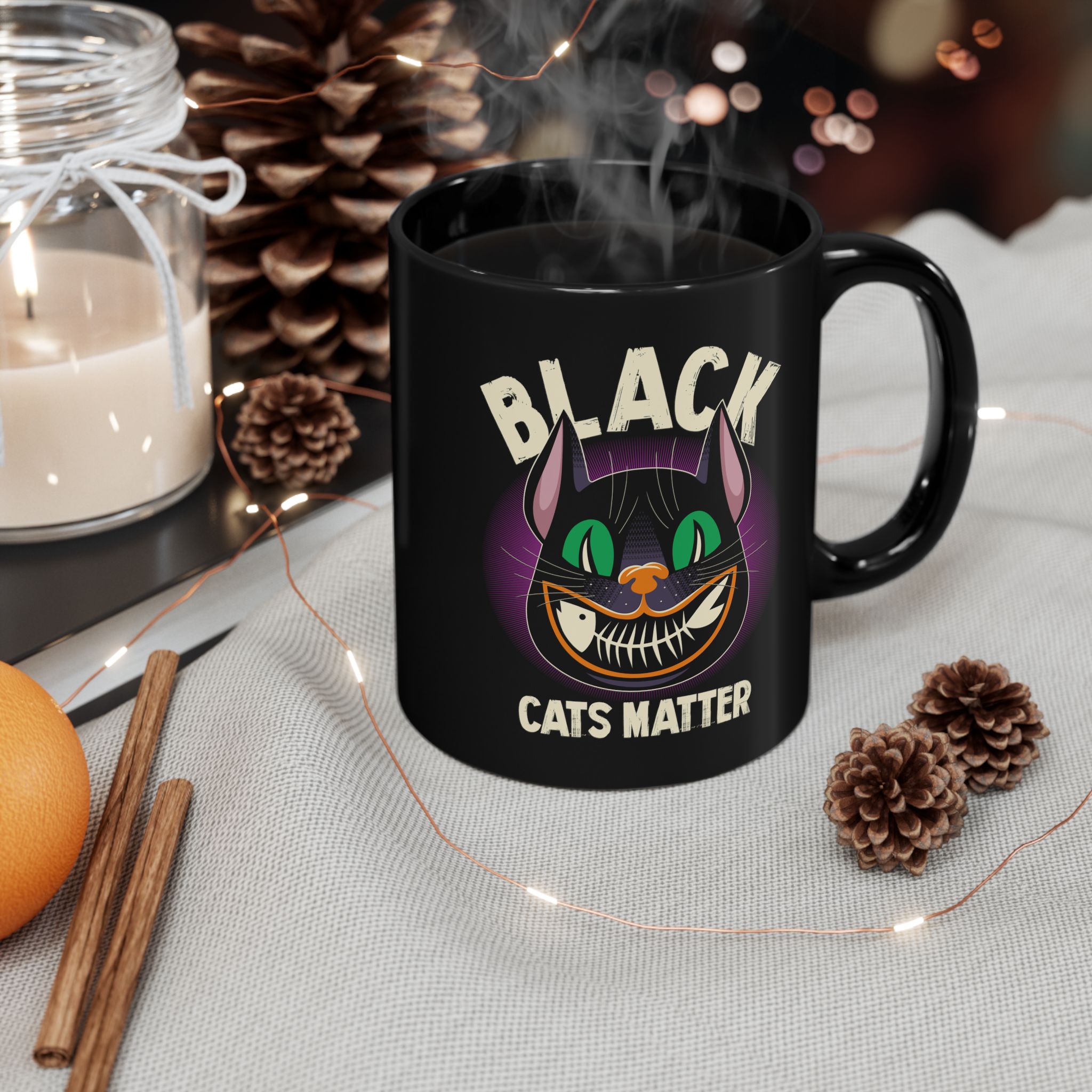 Glossy black ceramic mug showing a grinning black cat with huge green eyes, orange mouth outlines and a purple halo