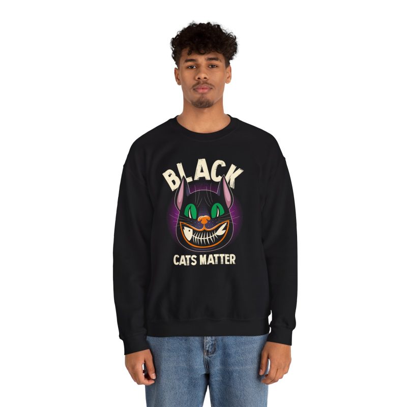 Person wearing a crewneck sweatshirt showing a grinning black cat with huge green eyes, orange mouth outlines and a purple halo