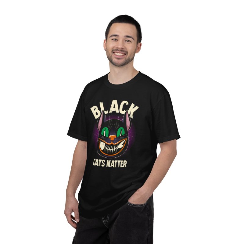 Person wearing a tee showing a grinning black cat with huge green eyes, orange mouth outlines and a purple halo