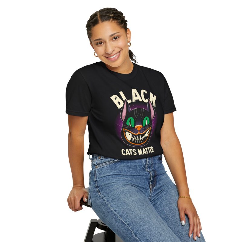 Person wearing a tee showing a grinning black cat with huge green eyes, orange mouth outlines and a purple halo