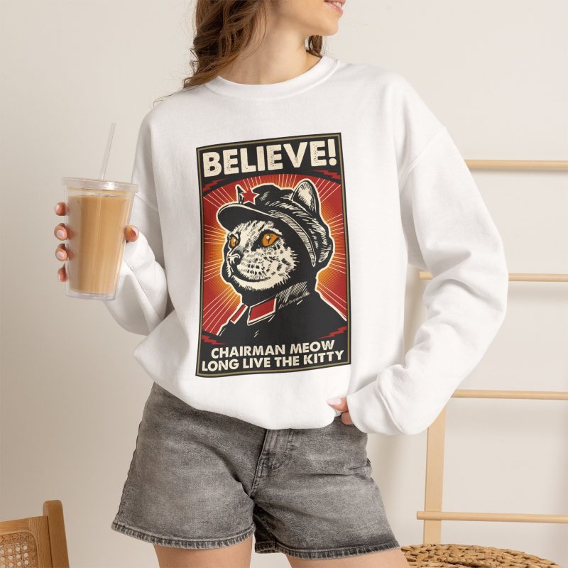 Person wearing a crewneck sweatshirt showing a stern black-and-cream cat in a red-star cap with orange-red sunburst rays and a black frame