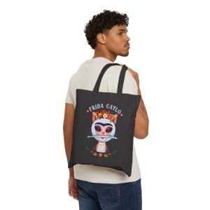 Person carrying a black canvas tote with a pale pink cat with a unibrow, a flower crown, gold beads and a teal fish facing outward