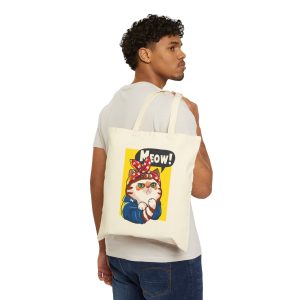 Person carrying a natural canvas tote with a white and ginger cat flexing its paw in a blue work shirt and red polka-dot bandana on a yellow panel facing outward