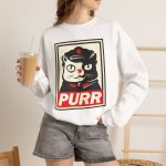 Person wearing a crewneck sweatshirt with a black and cream cat in a military cap with a red star above a red banner inside a double poster border printed on the front Person wearing a crewneck sweatshirt with a black and cream cat in a military cap with a red star above a red banner inside a double poster border printed on the front