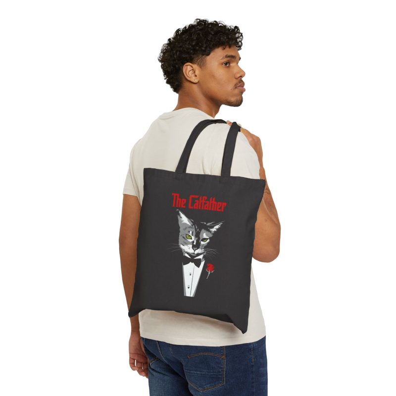 Person carrying a black canvas tote with a gray cat with green eyes in a white tuxedo shirt and black bow tie with a red rose facing outward