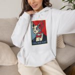 Person wearing a hoodie with a hairless cat in a suit and red bow tie printed on the front