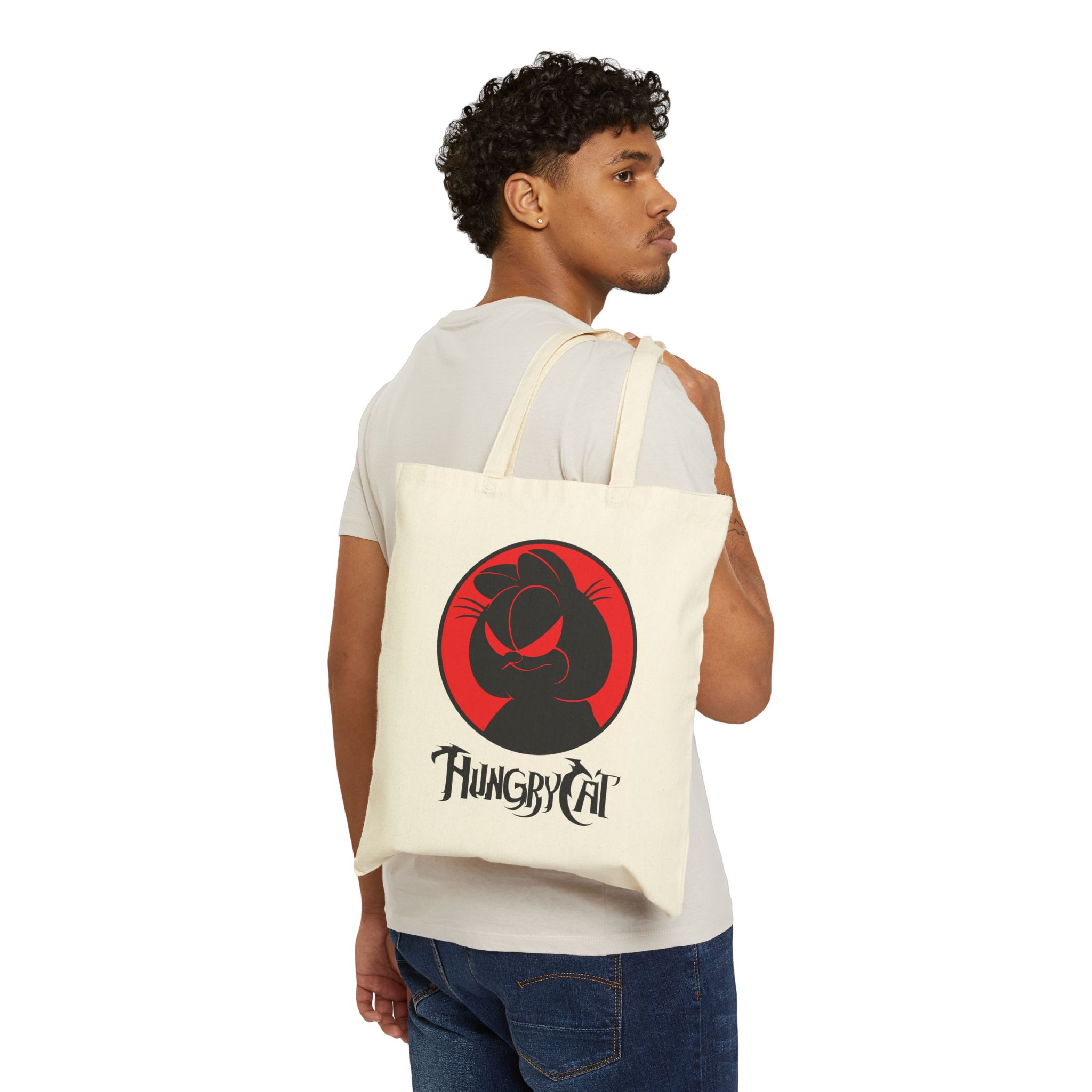 Person carrying a natural canvas tote with a sly black cat silhouette inside a red circle facing outward