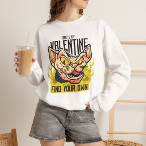 Person wearing a crewneck sweatshirt with a fierce hairless cat with yellow eyes and flames printed on the front