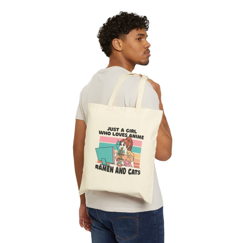 Person carrying a natural canvas tote showing a ramen-eating girl at a computer with three colorful cats