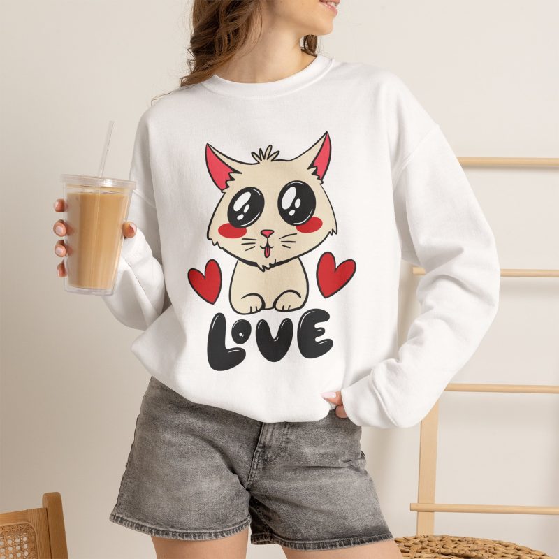 Person wearing a crewneck sweatshirt with a cream cat with glossy black eyes and red cheeks between two red hearts above black lettering printed on the front