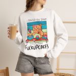 Person wearing a crewneck sweatshirt with a ginger baker cat with a pink whisk, cupcakes and turquoise retro stripes printed on the front Person wearing a crewneck sweatshirt with a ginger baker cat with a pink whisk, cupcakes and turquoise retro stripes printed on the front
