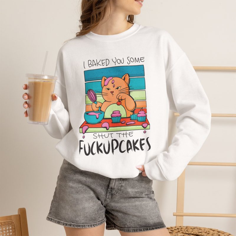 Person wearing a crewneck sweatshirt with a ginger baker cat with a pink whisk, cupcakes and turquoise retro stripes printed on the front