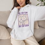 Person wearing a hoodie with a winking white cat drawn in blue inside a cream square with purple lettering printed on the front