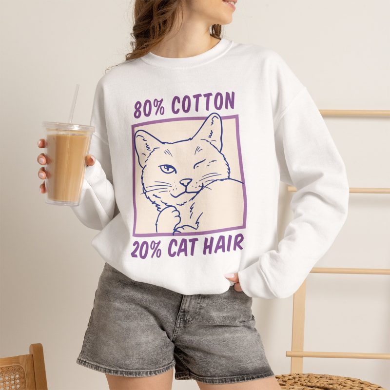 Person wearing a crewneck sweatshirt with a winking white cat drawn in blue inside a cream square with purple lettering printed on the front