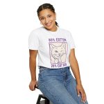 Person wearing a tee with a winking white cat drawn in blue inside a cream square with purple lettering printed on the front