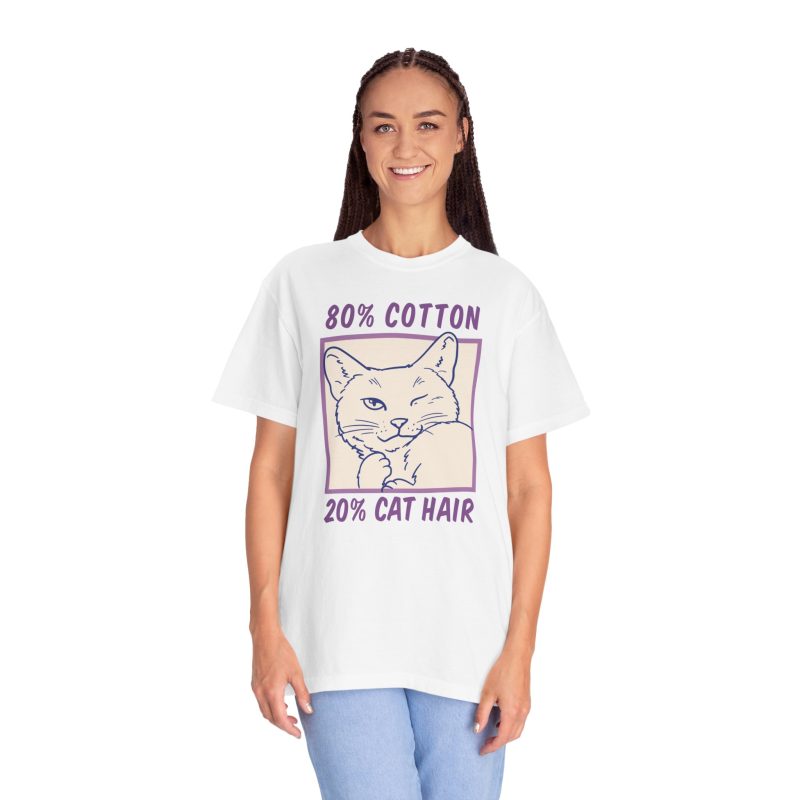 Person wearing a tee with a winking white cat drawn in blue inside a cream square with purple lettering printed on the front