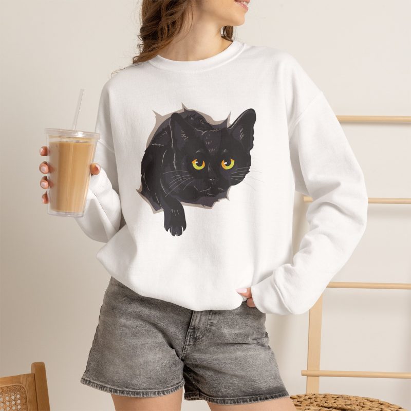 Person wearing a crewneck sweatshirt with an illustrated black cat with yellow-green eyes and a paw reaching through a gray torn-hole effect printed on the front