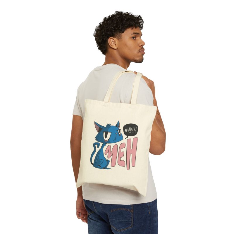 Person carrying a natural canvas tote showing an unimpressed blue cat beside large pink lettering and a black comic speech bubble