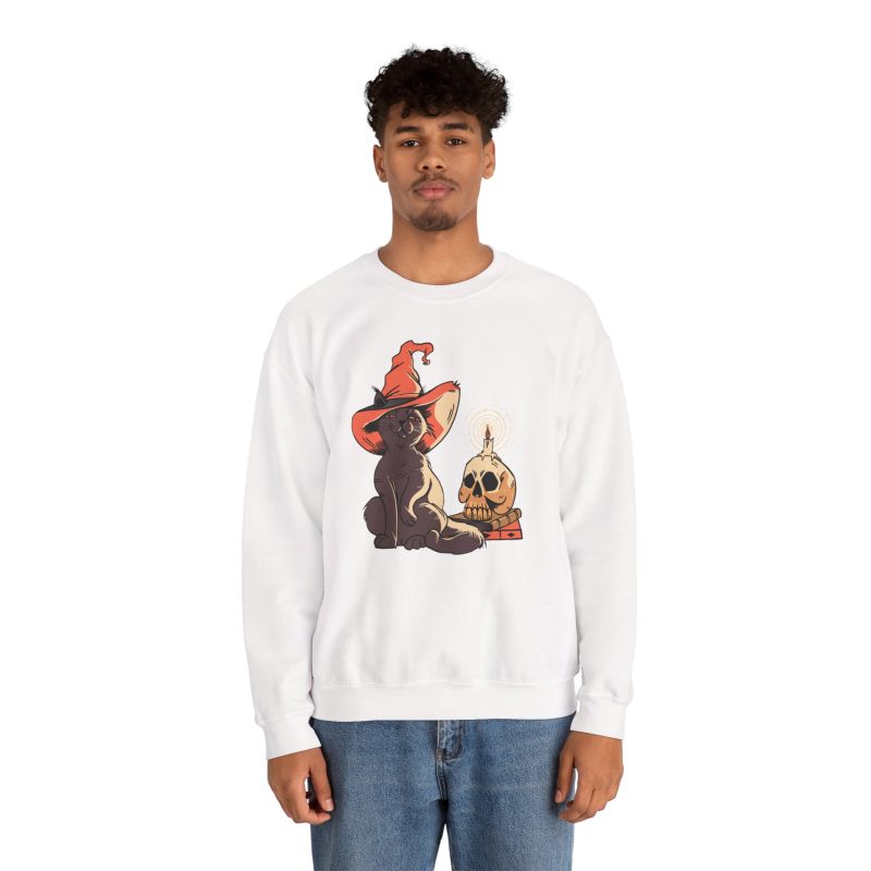 Person wearing a crewneck sweatshirt with a brown cat in an orange witch hat beside a skull, lit candle and stacked spell books printed on the front