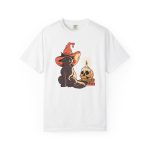 Front of the tee showing a brown cat in an orange witch hat beside a skull, lit candle and stacked spell books
