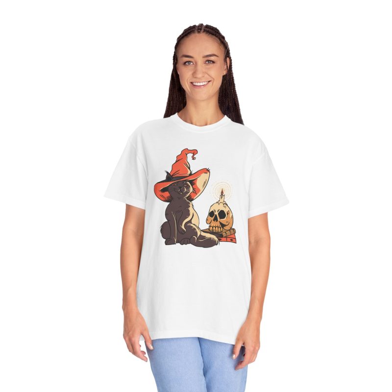 Person wearing a tee with a brown cat in an orange witch hat beside a skull, lit candle and stacked spell books printed on the front