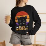 Person wearing a crewneck sweatshirt with a cat face inside red, orange and purple sunset stripes above warm orange lettering printed on the front