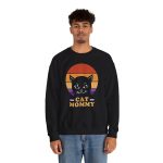 Person wearing a crewneck sweatshirt with a cat face inside red, orange and purple sunset stripes above warm orange lettering printed on the front