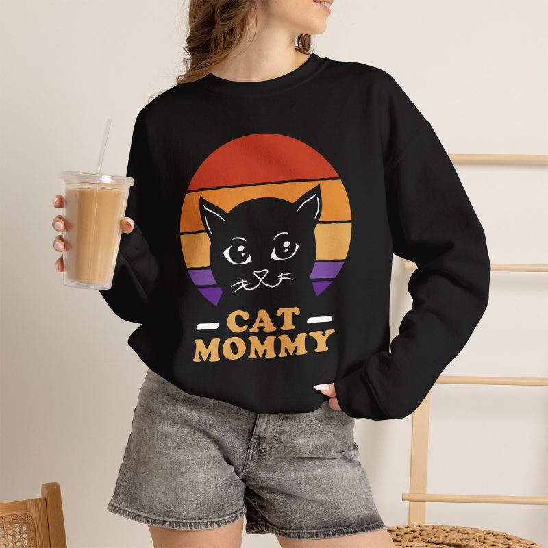 Person wearing a crewneck sweatshirt with a cat face inside red, orange and purple sunset stripes above warm orange lettering printed on the front