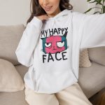 Person wearing a hoodie showing a pink and teal cat face and black lettering on the front