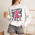 Person wearing a crewneck sweatshirt showing a pink and teal cat face and black lettering on the front