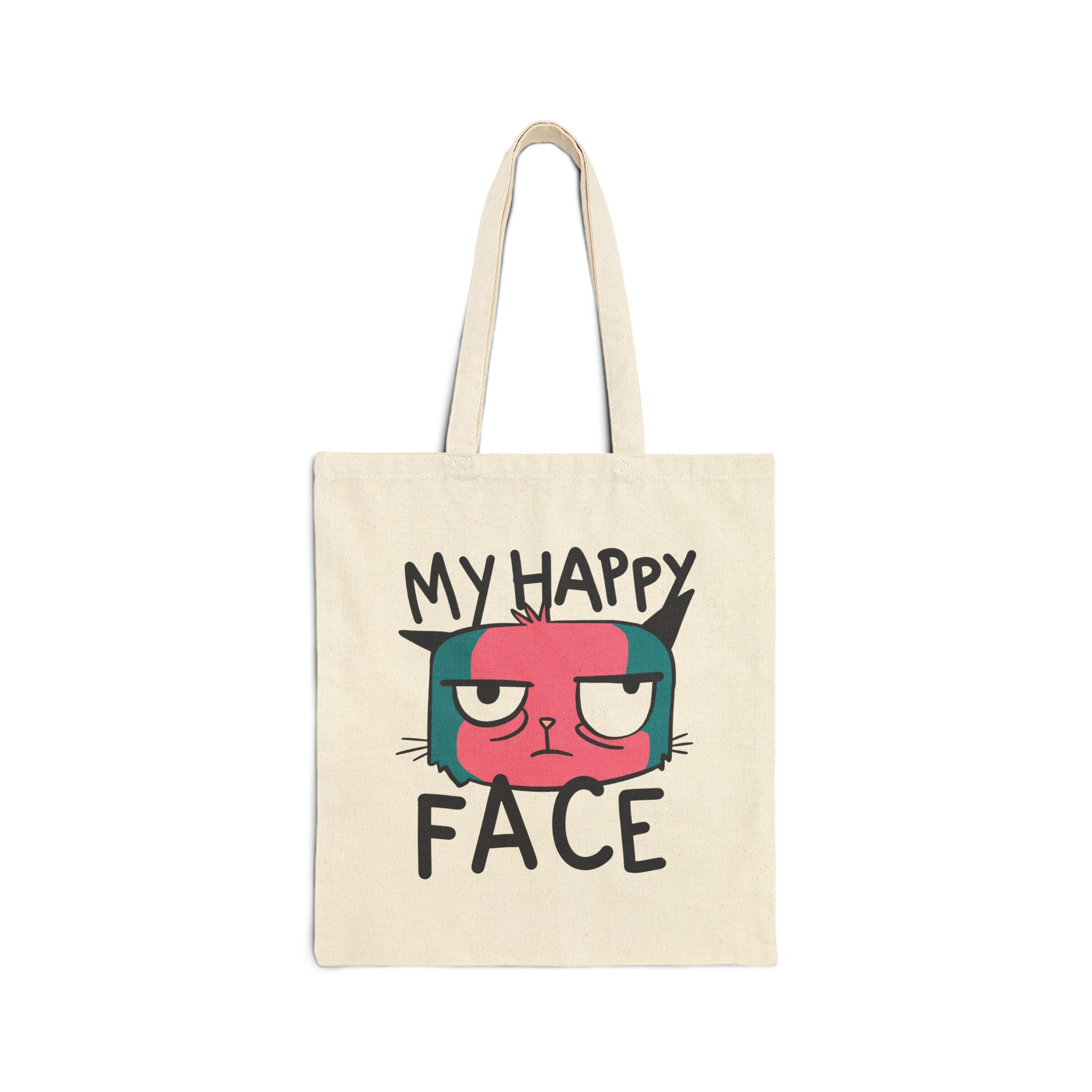 Front of the natural canvas tote showing a pink and teal cat face and black lettering