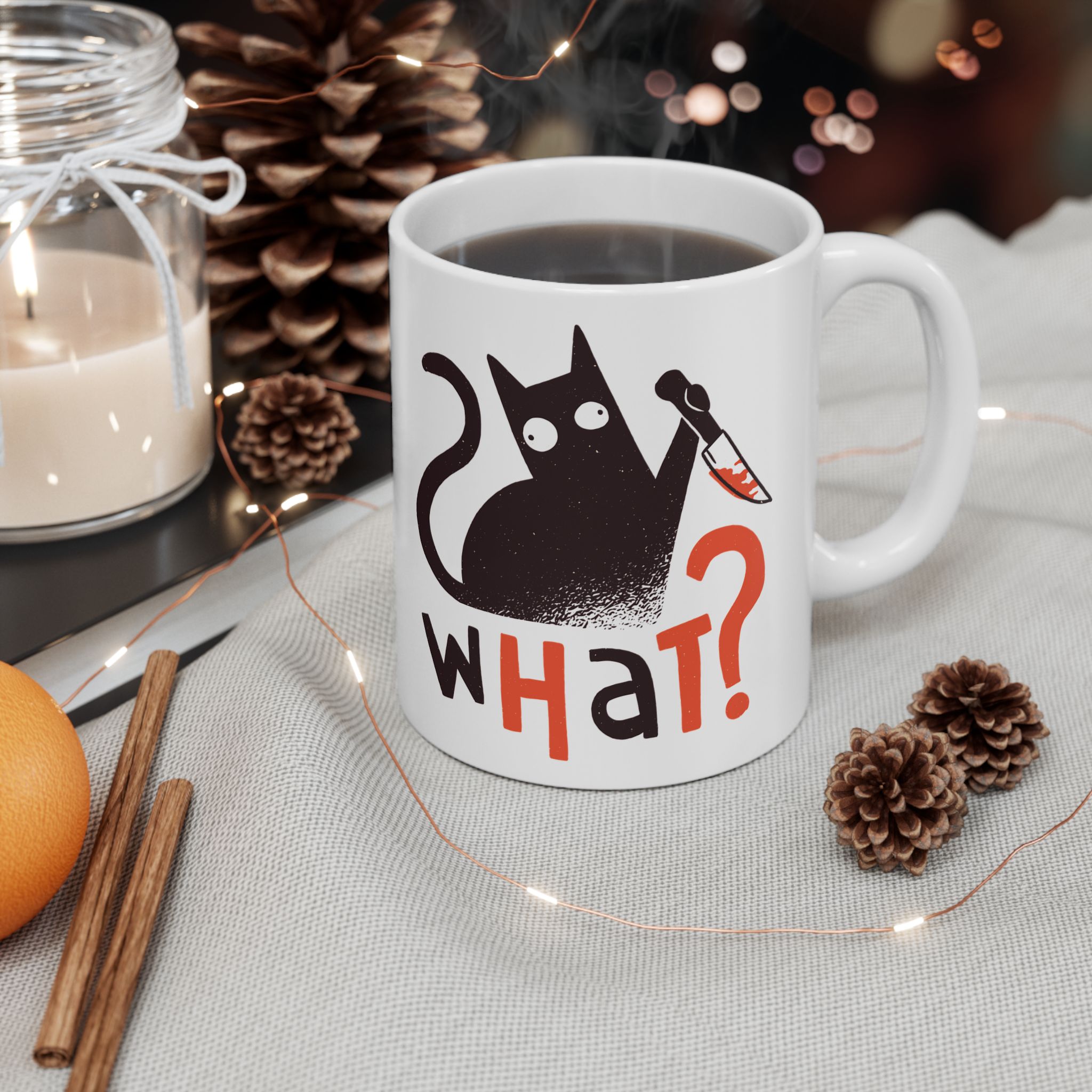 White ceramic mug showing a wide-eyed black cat with a kitchen knife and black and orange lettering