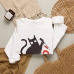 Wide-eyed black cat with a curled tail and kitchen knife beside black and orange WHAT? lettering in the front print Wide-eyed black cat with a curled tail and kitchen knife beside black and orange WHAT? lettering in the front print