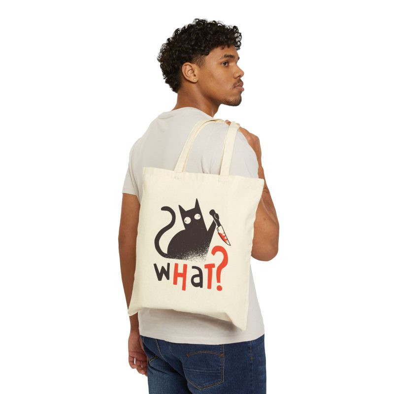 Person carrying a natural canvas tote with a wide-eyed black cat with a kitchen knife and black and orange lettering facing outward
