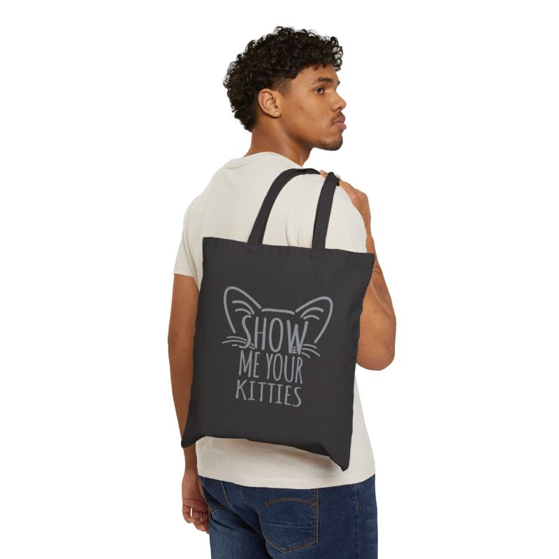 Person carrying a black canvas tote with gray cat-ear and whisker lettering facing outward