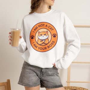 Person wearing a crewneck sweatshirt with an unimpressed ginger tabby with crossed arms inside an orange badge with dark purple lettering and two paw prints printed on the front