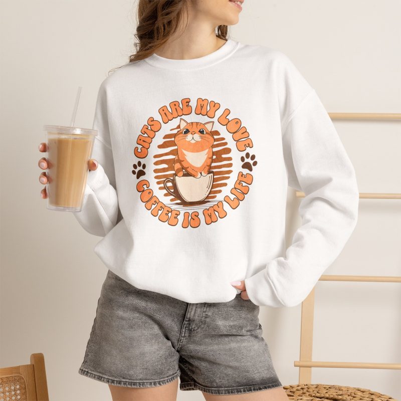 Person wearing a white crewneck sweatshirt with an orange tabby and coffee graphic