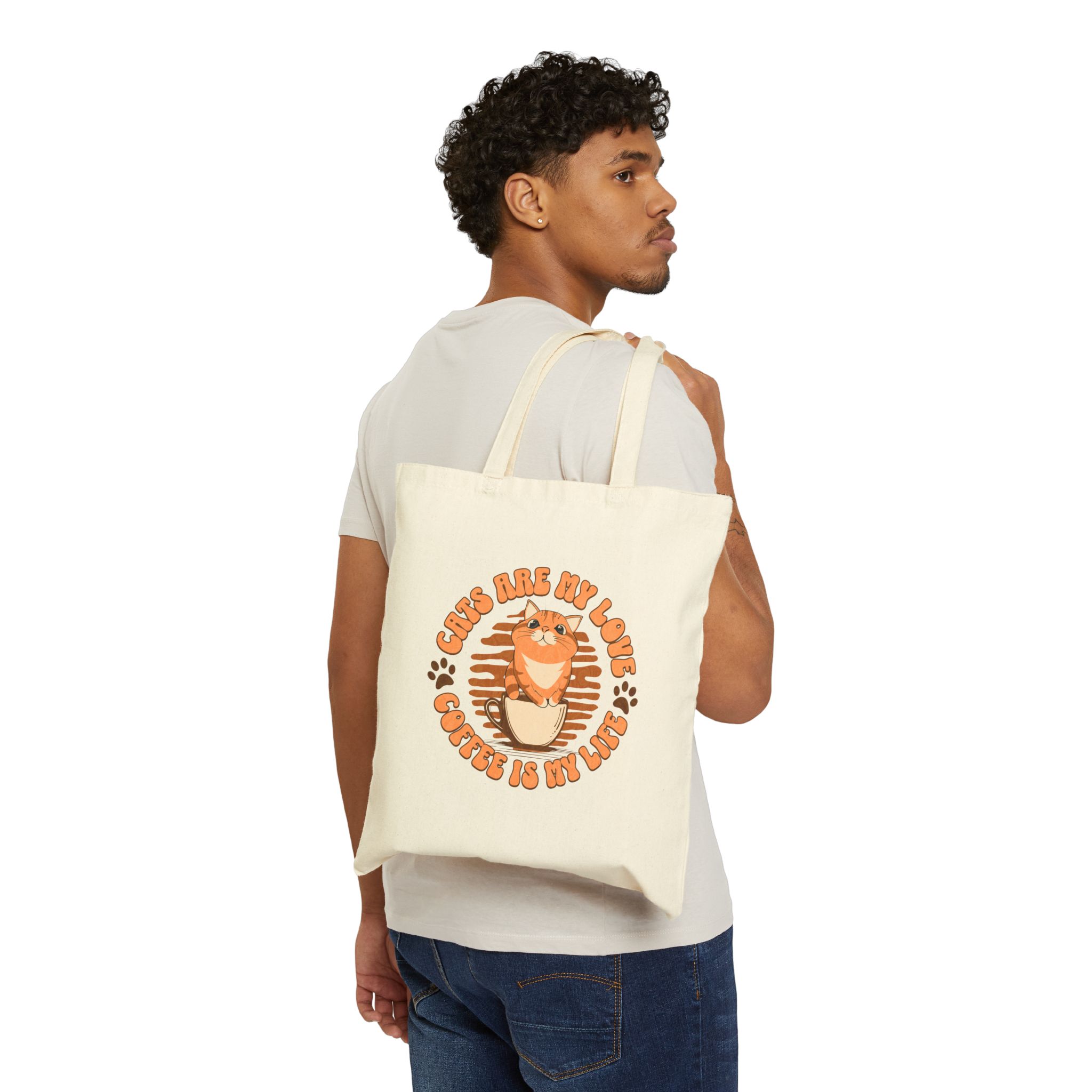 Person carrying a natural canvas tote with an orange tabby and coffee graphic facing outward