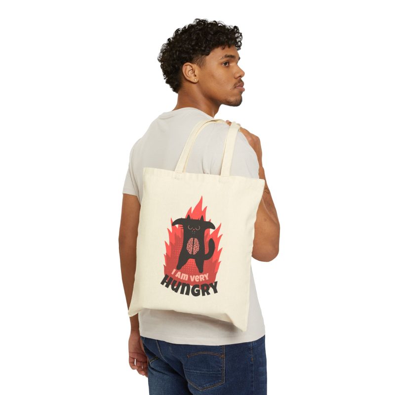 Person carrying a natural canvas tote with a hungry black cat and pink flames